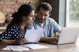 Eine Frau und ein Mann sehen auf Papiere und einen Laptop