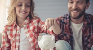 Ein Mädchen wirft mit ihrem Vater eine Münze in ein Sparschwein