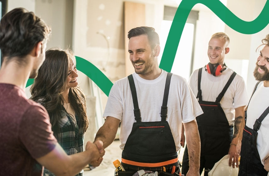 Bauherr und Handwerker schütteln sich die Hand. Ebenfalls auf dem Bild sind eine Frau sowie zwei weitere Handwerker in hellen Hemden und dunklen Latzhosen zu sehen.