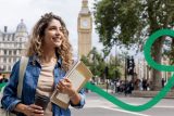 Eine junge Frau mit lockigem Haar hält in einer Hand einen Kaffeebecher und trägt in der anderen mehrere Bücher. Sie blickt sich fröhlich um, während im Hintergrund der berühmte Uhrturm Big Ben in London zu sehen ist.